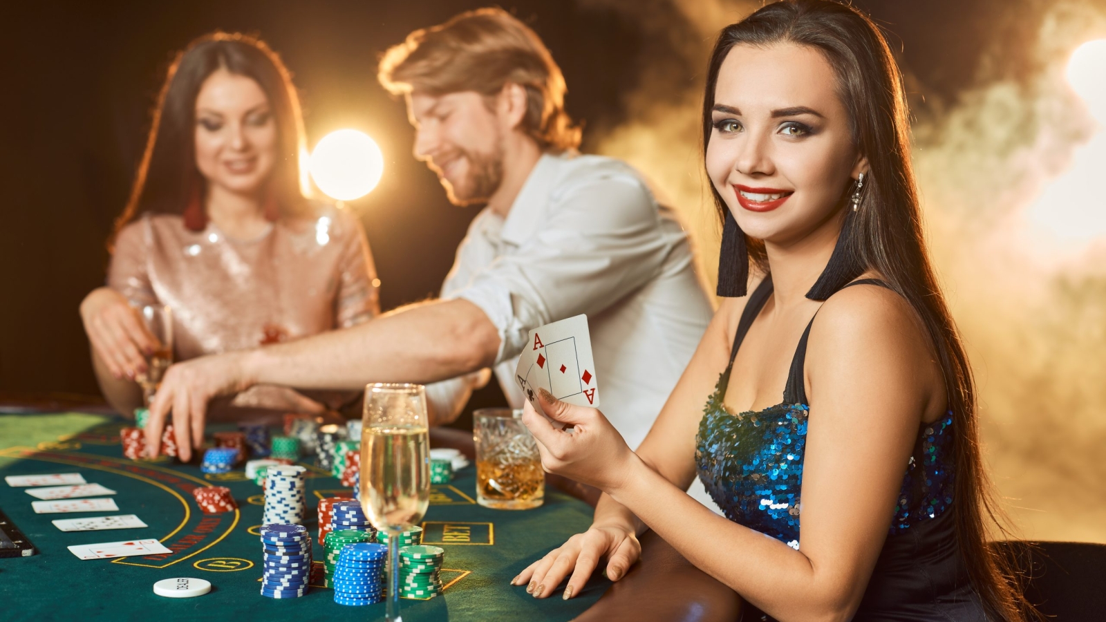 Group of an elegant people playing poker at the gambling house. Focus on a emotional brunette in a blue shiny dress. Passion, cards, chips, alcohol, dice, gambling, casino - it is entertainment. Dangerous fun card game for money. Smoke background.