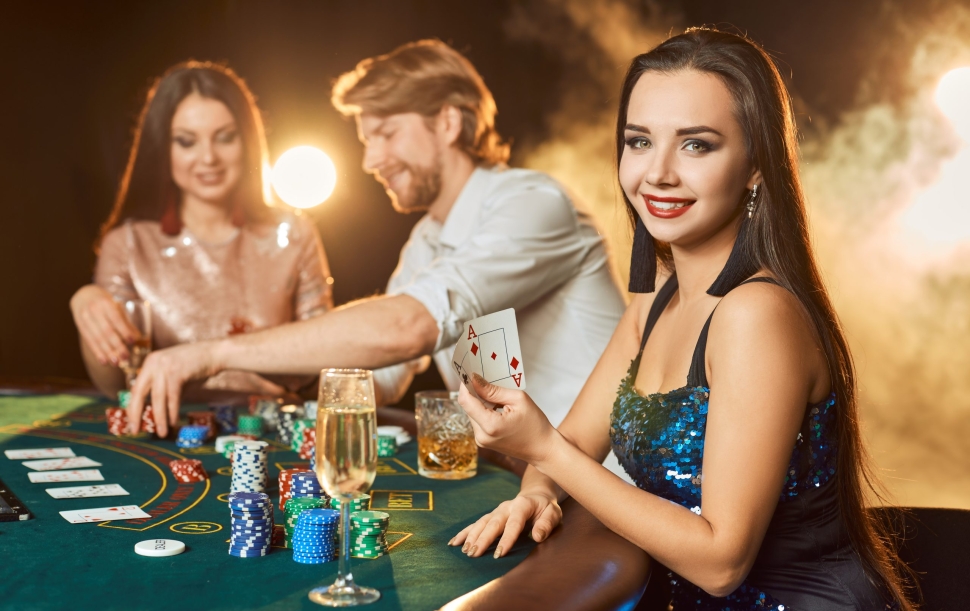 Group of an elegant people playing poker at the gambling house. Focus on a emotional brunette in a blue shiny dress. Passion, cards, chips, alcohol, dice, gambling, casino - it is entertainment. Dangerous fun card game for money. Smoke background.